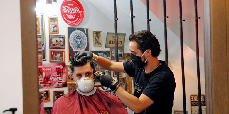 Seorang tukang potong rambut tengah memotong rambut pelanggan di kota Thessaloniki, Yunani, pada 4 Mei 2020. Yunani mulai memberlakukan pencabutan gradual lockdown untuk memerangi virus corona.