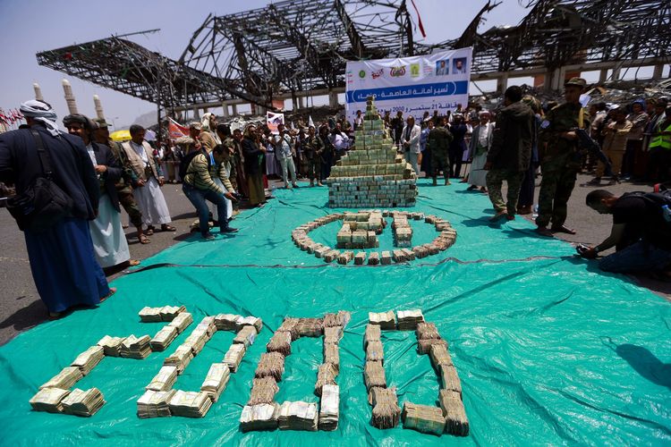 Seorang milisi kelompok pemberontak Houthi berjaga di samping tumpukan uang di ibu kota Sanaa, Yaman, pada 24 September 2020. Houthi memamerkan uang, makanan, dan sumbangan lainnya untuk merayakan 2.000 perlawanan mereka terhadap koalisi yang dipimpin Arab Saudi.