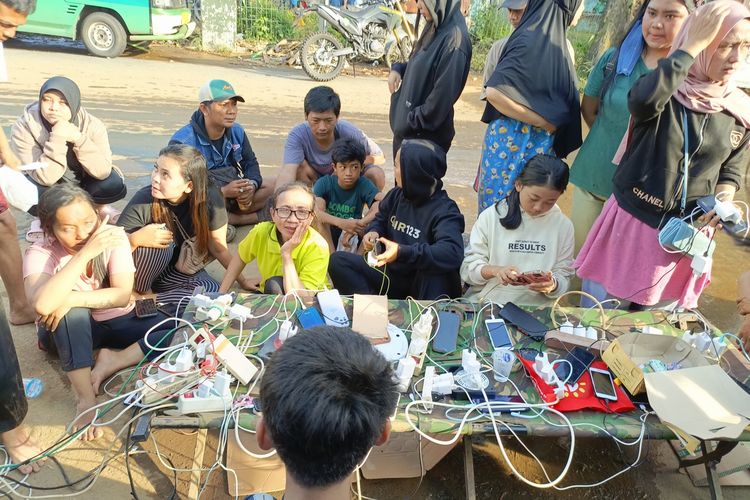 Puluhan warga Kampung Lamajang, Desa Citereup, Kecamatan Dayeuhkolot, Kabupaten Bandung mengantre untuk mengisi baterai HP miliknya di bengkel milik salah seorang warga yang membuka jasa charge HP, Jumat (12/1/2024)