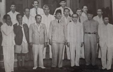 Menteri Penerangan Amir Sjarifuddin (depan, nomor dua dari kiri, mengenakan jas dan bercelana pendek), bersama Presiden Sukarno, Wapres Mohammad Hatta, dan menteri-menteri kabinet pertama, 4 Oktober 1945.