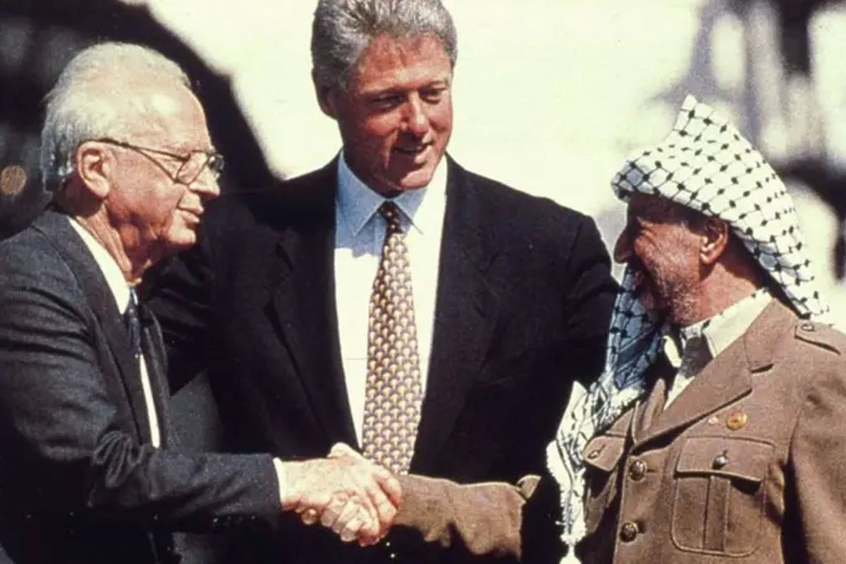 Presiden Amerika Bill Clinton menyaksikan Perdana Menteri Israel Yitzhak Rabin berjabat tangan dengan pemimpin Palestina Yasser Arafat di Gedung Putih setelah penandatanganan kesepakatan yang mengalihkan sebagian besar Tepi Barat ke kendali Palestina.