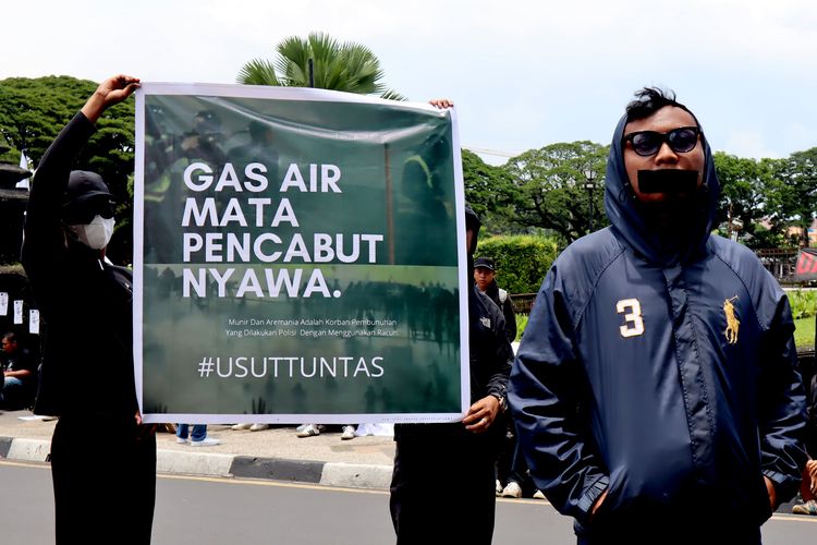 Suporter Arema FC, Aremania menutup mulut dan membentangkan banner saat melakukan aksi damai menuntut penegakan hukum yang adil terkait Tragedi Kanjuruhan yang menelan 133 korban meninggal di Kota Malang, Kamis (20/10/2022) pagi.
