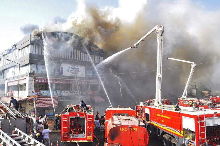 Mobil pemadam kebakaran menyemprotkan air ke gedung kampus yang terbakar di kota Surat, India barat, Jumat (24/5/2019).
