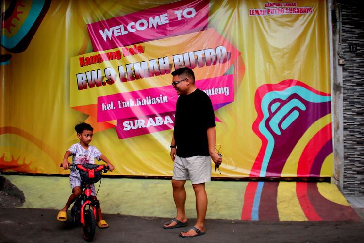 Seorang warga sedang ngobrol didepan banner untuk menyemarakan Piala Dunia U17 2023 Indonesia yang ada di Kampung Lemah Putro Jalan Embong Kaliasin Gang III dan IV, Kota Surabaya, Jawa Timur.
