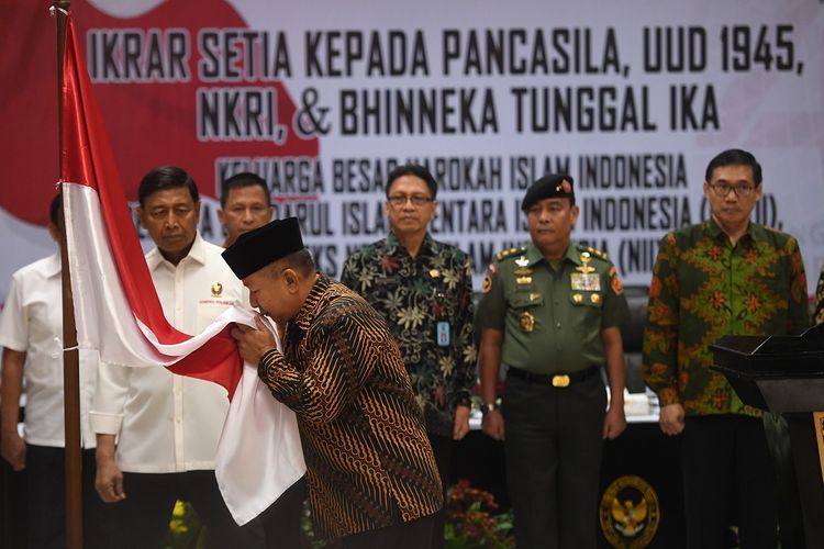 Menko Polhukam Wiranto (kiri) menyaksikan anak pemimpin Darul Islam/Tentara Islam Indonesia (DI/TII) Sekarmaji Marijan Kartosuwiryo, Sarjono Kartosuwiryo (kedua kiri) mencium bendera merah putih dalam acara pengucapan ikrar setia kepada Pancasila, UUD 45, NKRI dan Bhineka Tunggal Ika di Jakarta, Selasa (13/08/2019). Sebanyak 14 orang Keluarga Besar Harokah Islam Indonesia, mantan anggota Darul Islam/Tentara Islam Indonesia (DI/TII) dan mantan anggota Negara Islam Indonesia (NII) mengikuti pembacaan ikrar setia tersebut. ANTARA FOTO/Akbar Nugroho Gumay/nz.