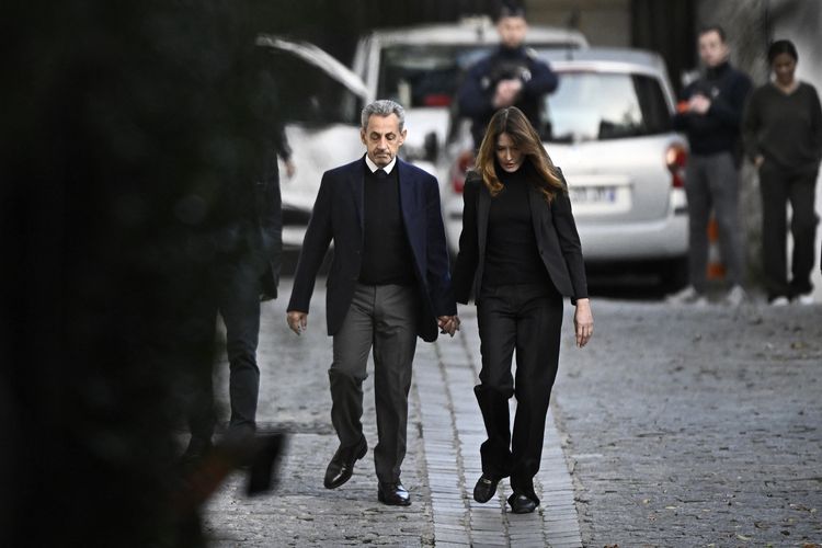 Mantan Presiden Perancis Nicolas Sarkozy (kiri) bergandengan tangan dengan istrinya, Carla Bruni- Sarkozy saat menuju penjara La Sante untuk menjalani masa tahanan lima tahun, Selasa (21/10/2025).