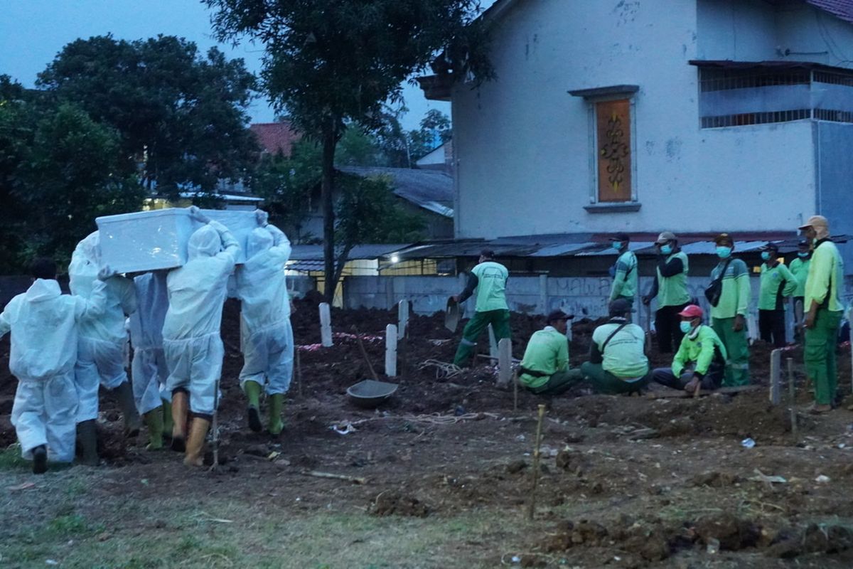 Petugas dengan menggunakan Alat Pelindung Dasar (APD) mengangkat peti jenazah pasien Covid-19 untuk dimakamkan di Taman Pemakaman Umum (TPU) Srengseng Sawah, Jagakarsa, Jakarta Selatan pada Jumat (15/1/2021). TPU Srengseng Sawah dijadikan sebagai tempat pemakaman jenazah pasien Covid-19 sejak Selasa (12/1/2021). TPU Srengseng Sawah memiliki lahan seluas 0,5 hektar dan bisa menampung sekitar 700 makam untuk jenazah pasien Covid-19.