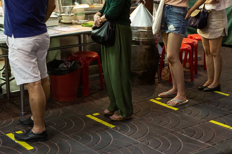 Terlihat garis-garis pembatas yang ditempel di perumukaan trotoar untuk membatasi jarak antar pembeli yang sedang mengantre membeli makanan di Yaowarat, Bangkok, Thailand