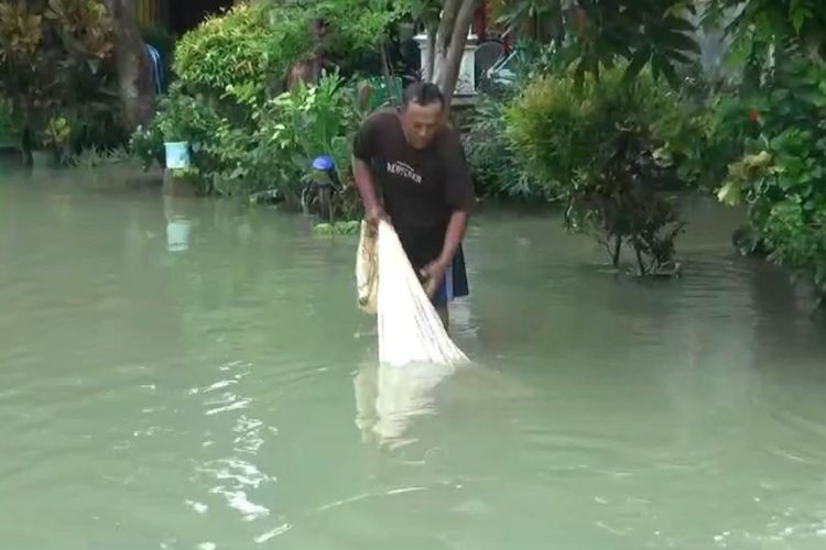Warga memanfaatkan momen banjir di Desa Tambakploso, Kecamatan Turi, Lamongan, Jawa Timur, dengan mencari ikan di jalan lingkungan depan rumahnya, Rabu (7/2/2024).