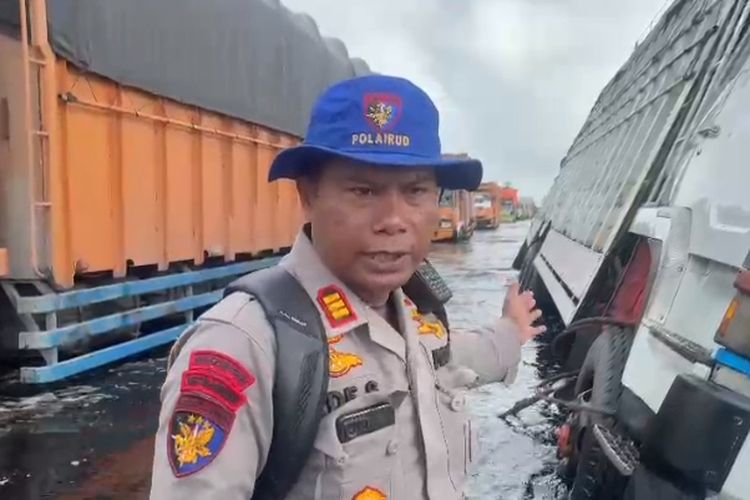 Petugas kepolisian saat berupaya mengevakuasi salah satu mobil truk yang terperosok di jalan lintas timur sumatera yang terendam air, di Kabupaten Pelalawan, Riau, Sabtu (6/1/2024).