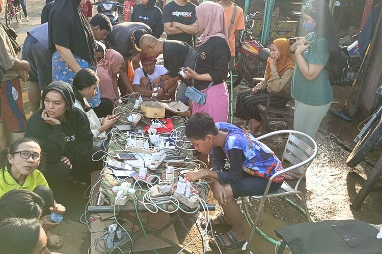 Puluhan warga Kampung Lamajang, Desa Citereup, Kecamatan Dayeuhkolot, Kabupaten Bandung mengantre untuk mengisi baterai ponsel di bengkel milik salah seorang warga yang membuka jasa pengisian daya, Jumat (12/1/2024).