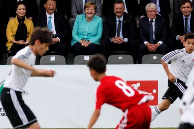 Xi Jinping dan Angela Merkel menyaksikan laga sepak bola remaja antara China dan Jerman saat berkunjung ke Berlin pada 2017.