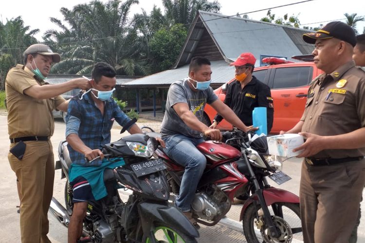 Camat Rupat Hanafi (kiri) dan Kepala BPBD Kabupaten Bengkalis Tajul Mudaris (topi merah) membagikan masker ke masyarakat untuk mengantisipasi dampak kabut asap di wilayah Kecamatan Rupat, Kabupaten Bengkalis, Riau, Senin (25/2/2019).