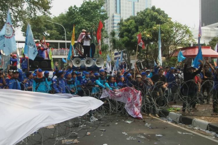 Massa buruh menarik kawat berduri untuk mendesak masuk ke depan Istana Negara di depan gedung Sapta Pesona, Jakarta Pusat, Senin (1/5/2017). Selain tarik-menarik kawat berduri, massa juga sempat melempar botol ke arah polisi yang berjaga.