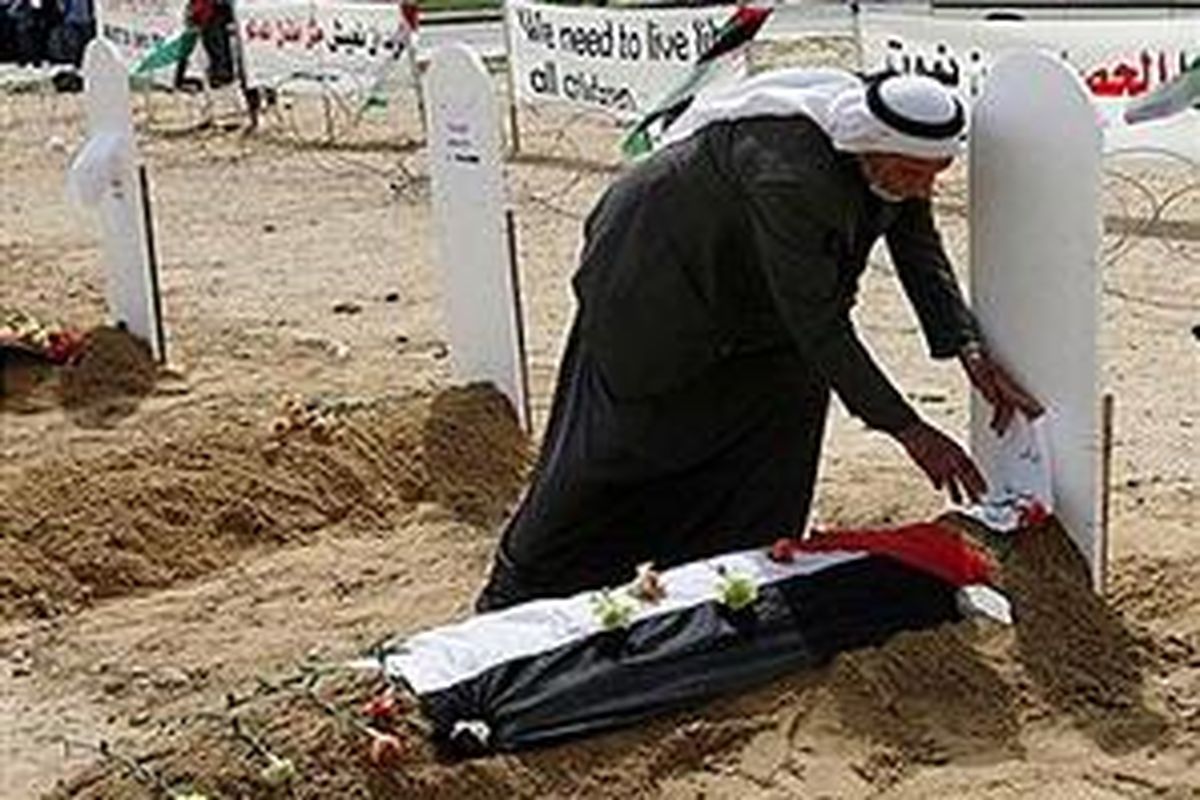 Seorang pria memasang bendera Palestina di atas kuburan palsu untuk menggambarkan nasib perekomian Gaza yang hancur akibat perang.