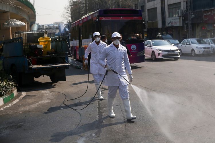 Petugas kesehatan mengenakan masker dan pakaian pelindung menyemprotkan disinfektan di jalanan Teheran, Iran, pada 5 Maret 2020 sebagai pencegahan terhadap virus corona.