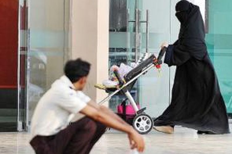 Seorang perempuan Arab Saudi melintasi seorang pekerja asing di pintu masuk sebuah mal di Riyadh, Kamis (7/11). Pemerintah Arab Saudi mulai memulangkan ribuan pekerja asing ilegal yang kebanyakan mengisi pasar pekerja kasar. 
