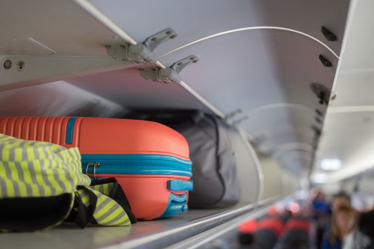 Bagasi jinjing di rak paling atas di atas kepala di pesawat, penumpang menempatkan tas di kompartemen kabin.