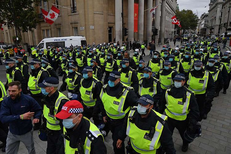Barisan polisi bermasker mengawal pengunjuk rasa yang menggelar aksi menentang aturan pembatasan yang dikeluarkan pemerintah PM Inggris terkait penyebaran Covid-19, di Trafalgar Square di London, Inggris, Sabtu (26/9/2020). Aksi yang diikuti ribuan warga tersebut di antaranya menolak kebijakan lockdown, vaksinasi, dan kewajiban penggunaan masker.