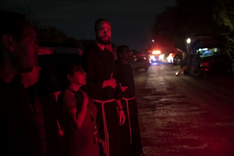 Pendeta lokal dari Keuskupan Agung San Antonio berdiri di dekat lokasi di mana sebuah trailer traktor ditemukan dengan para migran di dalam di luar San Antonio, Texas pada 27 Juni 2022. Sedikitnya 46 migran ditemukan tewas pada 27 Juni 2022 di dalam dan sekitar sebuah traktor- trailer yang ditinggalkan di pinggir jalan di pinggiran kota San Antonio di Texas. 