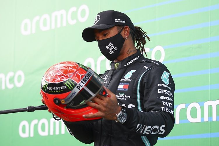 Pebalap Mercedes, Lewis Hamilton, saat memegang helm kemenangan Michael Schumacher. Dia meraih helm tersebut setelah menyamai rekor kemenangan Schumacher.