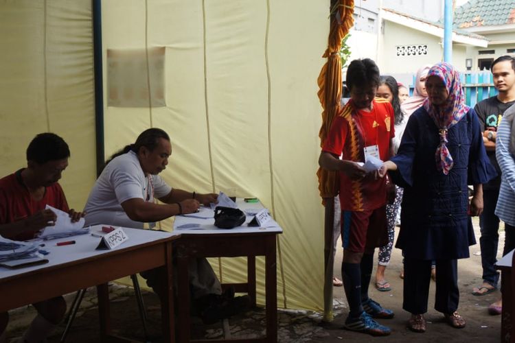 Dengan berpakaian lengkap sepatu sepak bola dan kostum timnas berbagai negara yang ikut serta dalam Piala Dunia 2018, para petugas KPPS di TPS 14 Kelurahan Karawang Kulon seolah menjadi pemain yang menggiring warga ke bilik suara yang dihias bak tiang gawang.