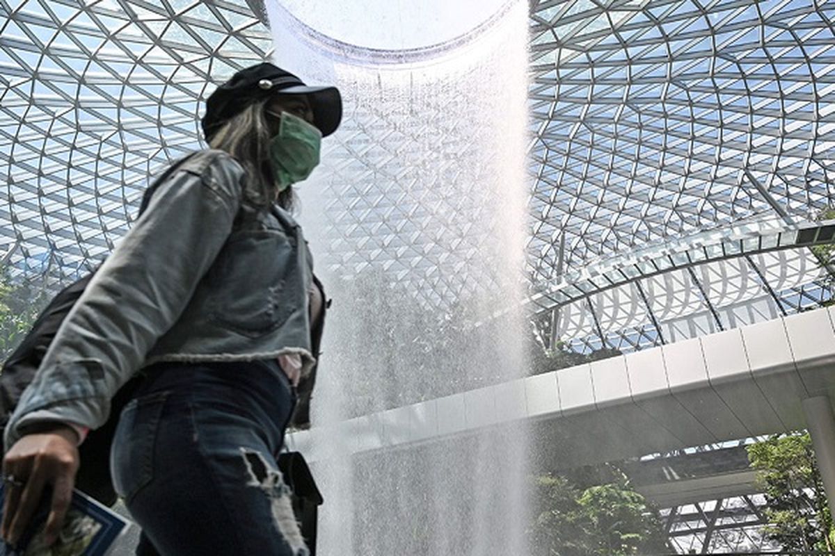 Seorang pengunjung terlihat memakai masker ketika melintas di depan air terjun Rain Vortex di Jewel yang berlokasikan di Bandara Internasional Changi