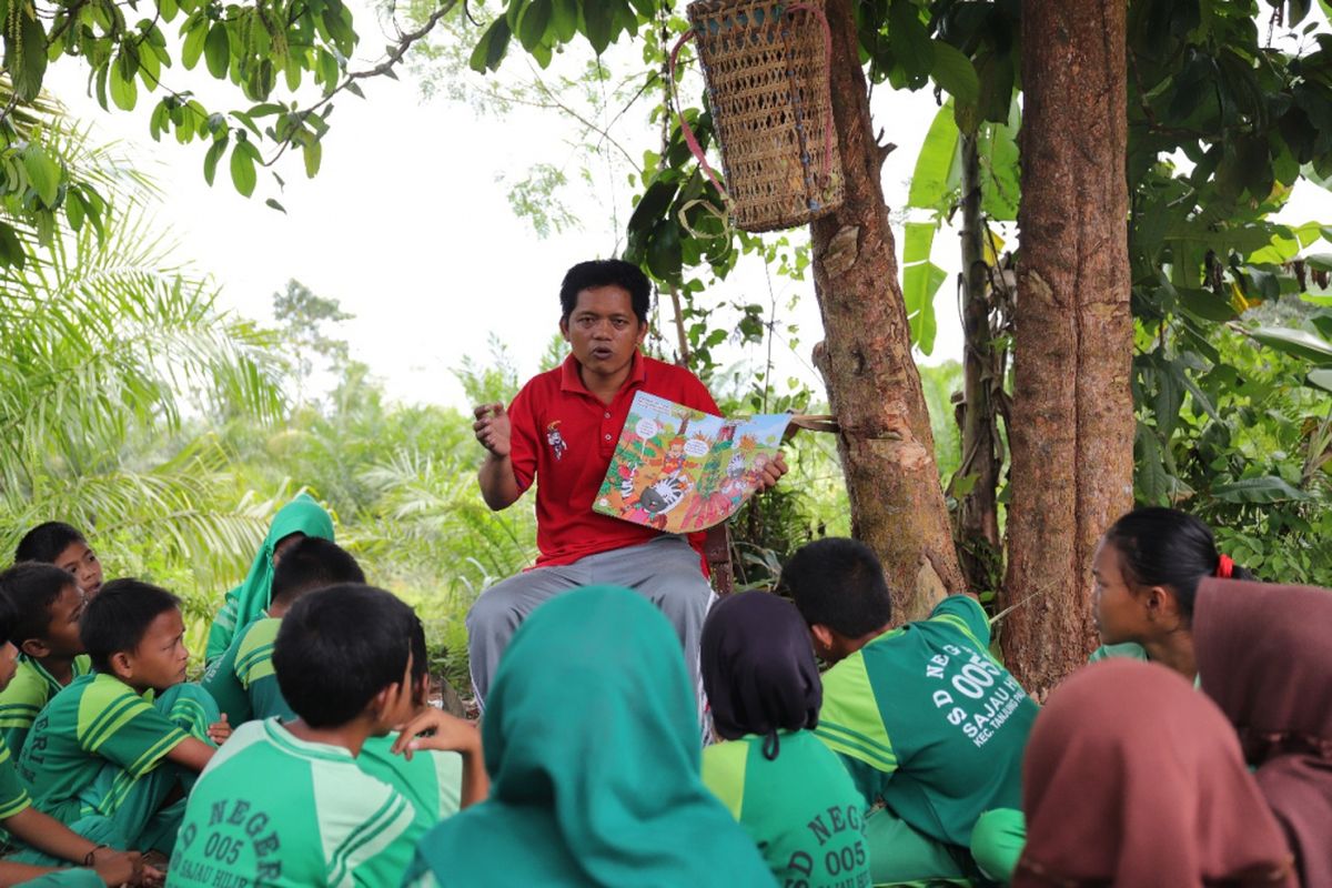 Yosep membacakan cerita kepada anak-anak di ladang sekolah, disela-sela waktu istirahat. Yosep merawat nasionalisme di pedalaman Kaltara dengan mendekatkan buku kepada anak.