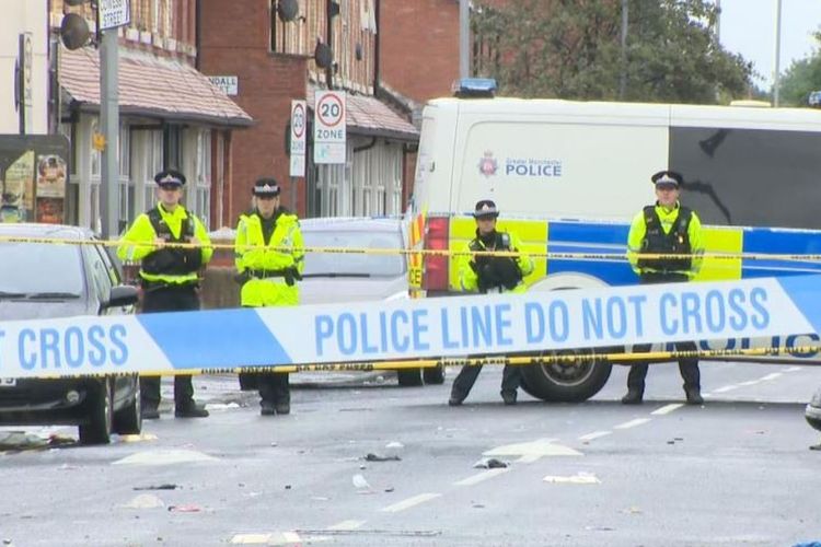 Petugas kepolisian Manchester berjaga di dalam garis polisi yang dipasang di Claremont Road, Moss Side, Manchester, Inggris, usai terjadinya insiden penembakan yang melukai 10 orang, Sabtu (11/8/2018).