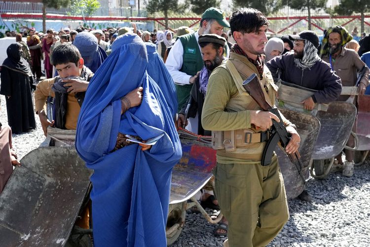 Seorang milisiTaliban berjaga-jaga ketika orang-orang menunggu untuk menerima jatah makanan yang didistribusikan oleh kelompok bantuan kemanusiaan Saudi, di Kabul, Afghanistan, Senin, 25 April 2022.