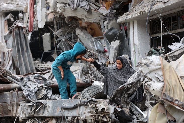 Seorang perempuan Palestina membantu seorang anak bermain di reruntuhan bangunan yang hancur akibat pengeboman Israel sebelumnya di Kota Gaza pada 8 April 2024, di tengah konflik yang sedang berlangsung antara Israel dan kelompok militan Hamas Palestina. Jelang Idul Fitri 2024, warga Gaza masih kekurangan bantuan.