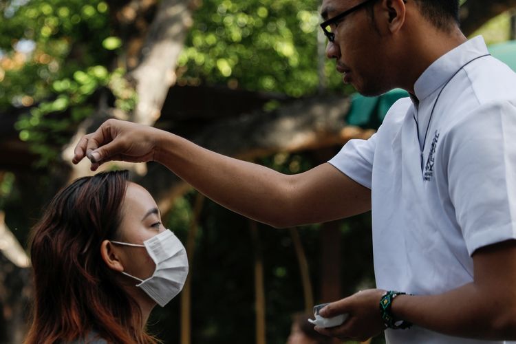 Seorang umat Katolik yang mengenakan masker mendapat taburan abu dari prodiakon gereja Katolik di National Shrine of Our Mother of Perpetual Help, Paranaque City, Metro Manila, pada 26 Februari 2020. Gereja Katolik setempat memutuskan mengubah ritual Rabu Abu demi mencegah wabah virus corona.