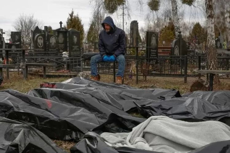 Seorang pegawai layanan pemakaman duduk di sebelah mayat-mayat warga sipil di Bucha.

