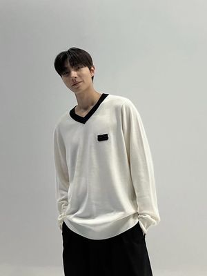 Hwang In Yeop mengenakan sweater lengan panjang berwarna putih dengan aksen garis hitam di bagian kerah.