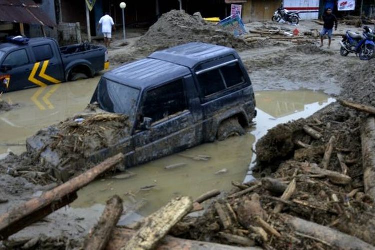 Kondisi rumah dan mobil yang tertimbun lumpur akibat terjangan banjir bandang di Kecamatan Masammba, Kabupaten Luwu Utara, Sulawesi Selatan, Rabu (15/07). Setelah banjir bandang melanda, beberapa warga menyaksikan banyaknya potongan kayu besar memenuhi sungai.