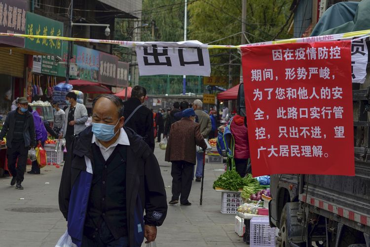 Seorang pria memakai masker berjalan melewati tulisan aturan jalan satu arah untuk mencegah penyebaran Covid-19 di kota Lanzhou, provinsi Gansu, China, pada Senin (25/10/2021).