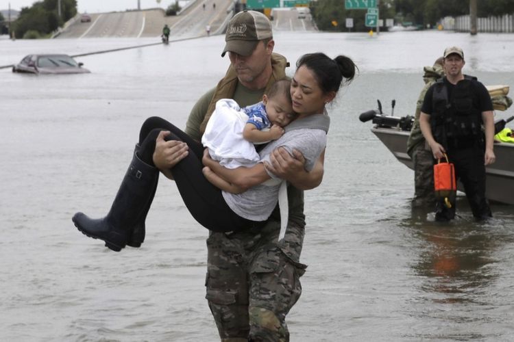 Daryl Hudeck, seorang polisi Houston, Texas, AS, menggendong Catherine Pham dan putranya, Aiden, berusia 13 bulan dalam sebuah proses evakuasi untuk menyelamatkan ibu dan anak itu dagi genangan banjir akibat badai Harvey, Minggu (27/8/2017).