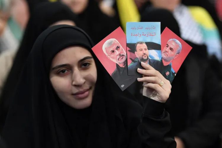 Seorang perempuan membawa foto pejabat pemimpin pasukan Irak Abu Mahdi Al Muhandis (kiri), wakil pemimpin Hamas Saleh Al Arouri (tengah), dan komandan tinggi Iran Qasem Soleimani (kanan).