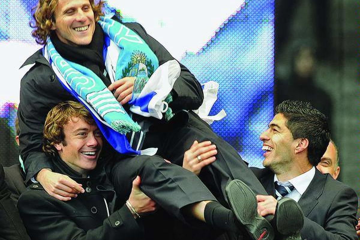 Striker Uruguay, Diego Forlan (tengah), dibopong oleh rekannya, Diego Lugano (kiri) dan Luis Suarez, pada acara penyambutan tim di Montevideo, Uruguay, Selasa (13/7). FIFA menganugerahi Forlan penghargaan Bola Emas untuk penampilannya di Piala Dunia 2010.