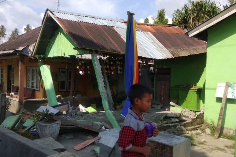 Seorang anak melintas di depan rumah yang roboh akibat gempa di Donggala, Sulawesi Tengah, Jumat (28/9/2018).