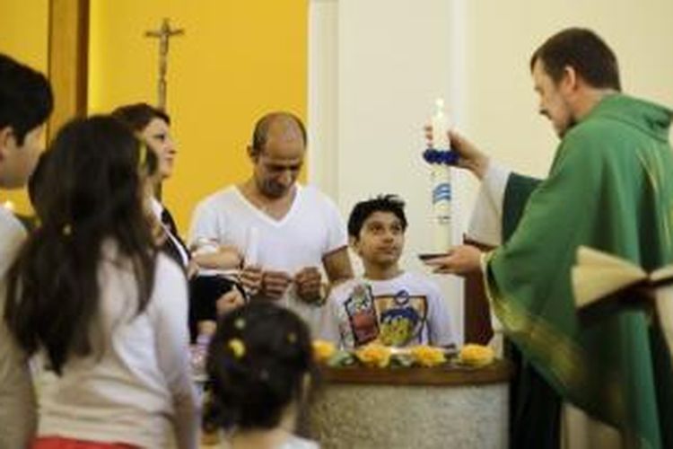 Pria asal Iran, Mohammed Ali Zonoobi (kaus putih) tengah menjalani ritual pembabtisan di sebuah gereja di Berlin, Jumat (4/9/2015). Zonoobi adalah satu dari ratuan pengungsi asal Iran dan Afganistan yang memilih untuk memeluk Kristen demi memperbesar peluang mereka diterima di Jerman.