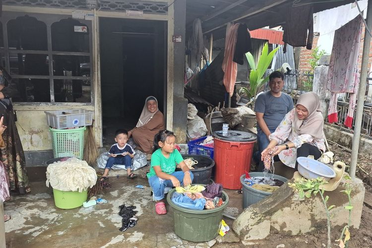 Nenek Arbiyah (duduk di pintu) bercengkrama dengan kerabatnya yang mencuci pakaian yang kotor terkena banjir. 