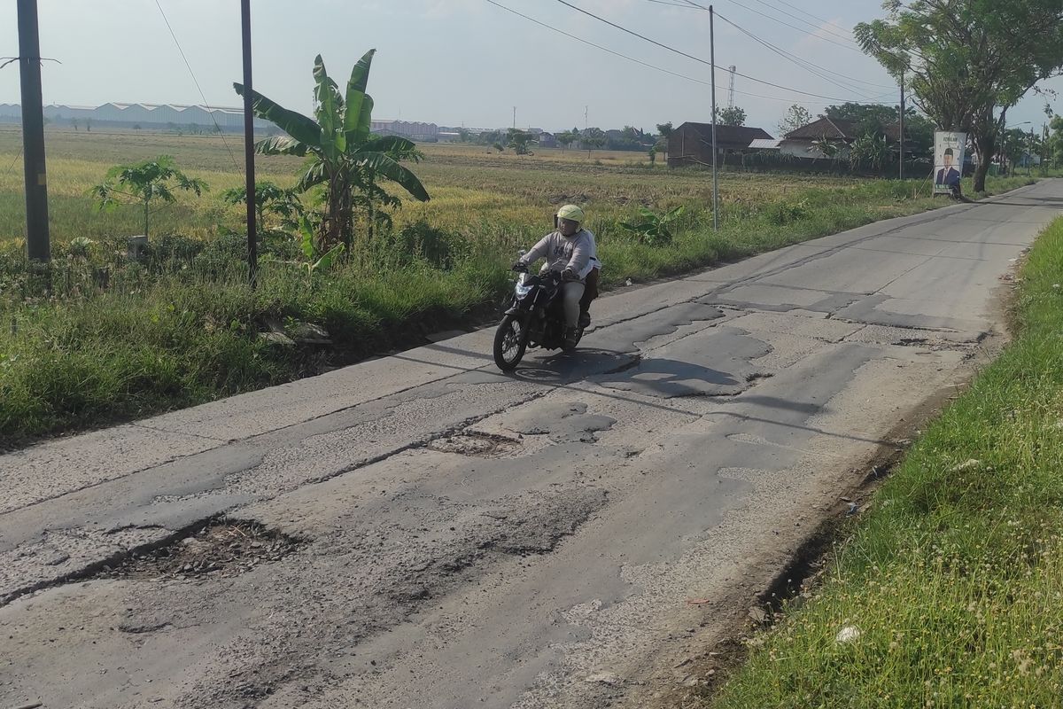 Seorang pemotor nampak hati-hati menghindari lubang di jalan Desa Ngemplik Wetan, Kecamatan Karanganyar, Kabupaten Demak, Minggu (4/8/2024). (KOMPAS.COM/NUR ZAIDI)