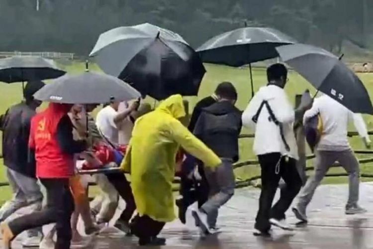 Tangkap layar gambar yang diambil dari lokasi kejadian menunjukkan kru penyelamat membawa calon pengantin pria, yang tersambar petir, dengan tandu di tengah hujan lebat, mengenakan jas hujan dan payung.
