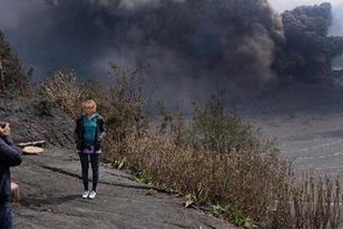 Wisatawan berpose dengan latar belakang Gunung Bromo yang masih menyemburkan abu vulkanik yang disertai suara letusan, Sabtu (22/1/2011). Status Gunung Bromo masih siaga dan terus dalam pantauan penuh. 