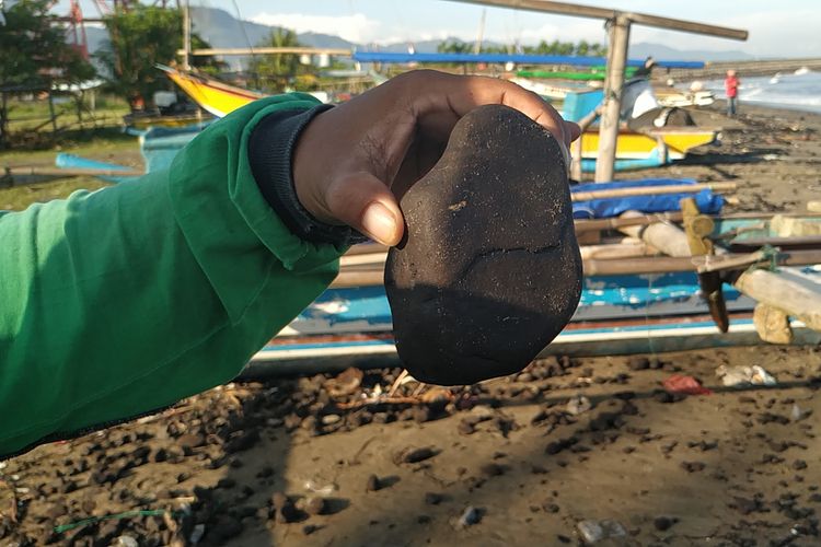 Seorang nelayan memperlihatkan batubara yang berasal dari tumpahan dua tongkang terdampar di Pantai Batu Bintang, Cipatuguran, Palabuhanratu, Sukabumi, Jawa Barat, Kamis (9/5/2019)