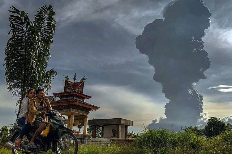 Pengendara melintas dengan latar belakang Gunung Sinabung menyemburkan material vulkanik saat erupsi, di Karo, Sumatera Utara, Minggu (9/6/2019). Gunung Sinabung berstatus Siaga (Level III) kembali mengalami erupsi dengan tinggi kolom abu mencapai 7.000 meter dan menyebabkan sejumlah desa tertutup debu vulkanik.