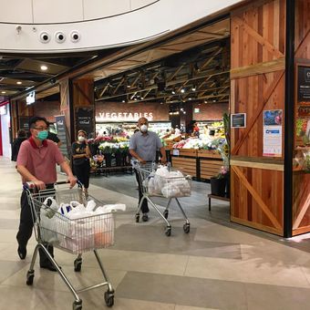 Warga memakai masker mendorong troli belanja meninggalkan Supermarket Cold Storage, Great World City, Singapura Tengah, Senin sore (20/04/2020).