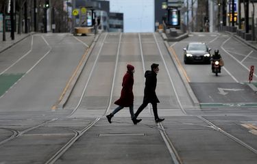 Pejalan kaki berjalan melintasi jalan yang sepi di kota Melbourne, Australia, pada 24 Juli 2021, hari kesembilan lockdown.