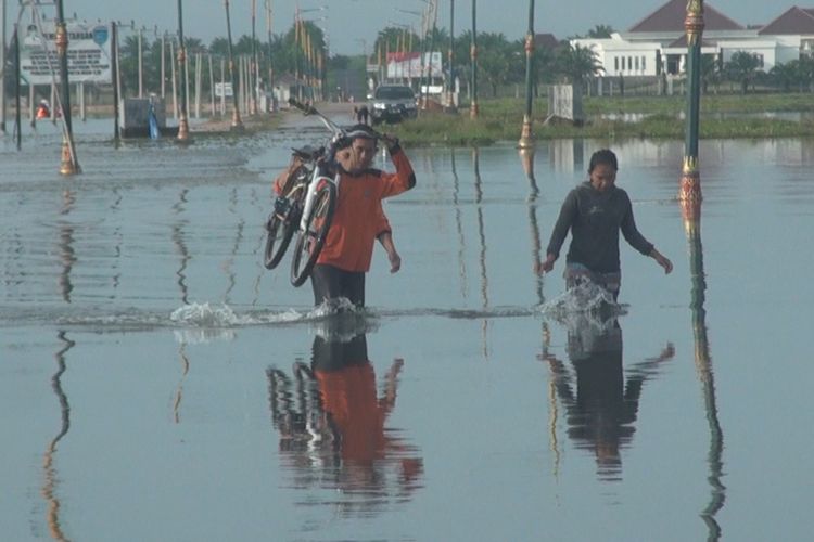 Tak kuat menahan derasnya arus banjir di jalan menuju kompleks perkantoran Pemkab Ogan Ilir, seorang pesepeda perempuan harus dibantu dua personel BPBD Ogan Ilir, Senin (19/3/2018).